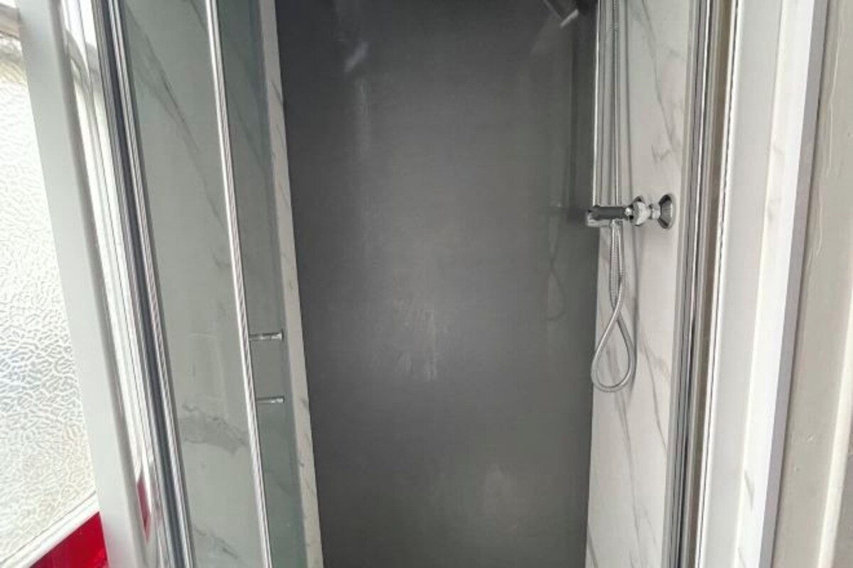 Un baño con puerta de vidrio, ducha y pared de mármol blanco.