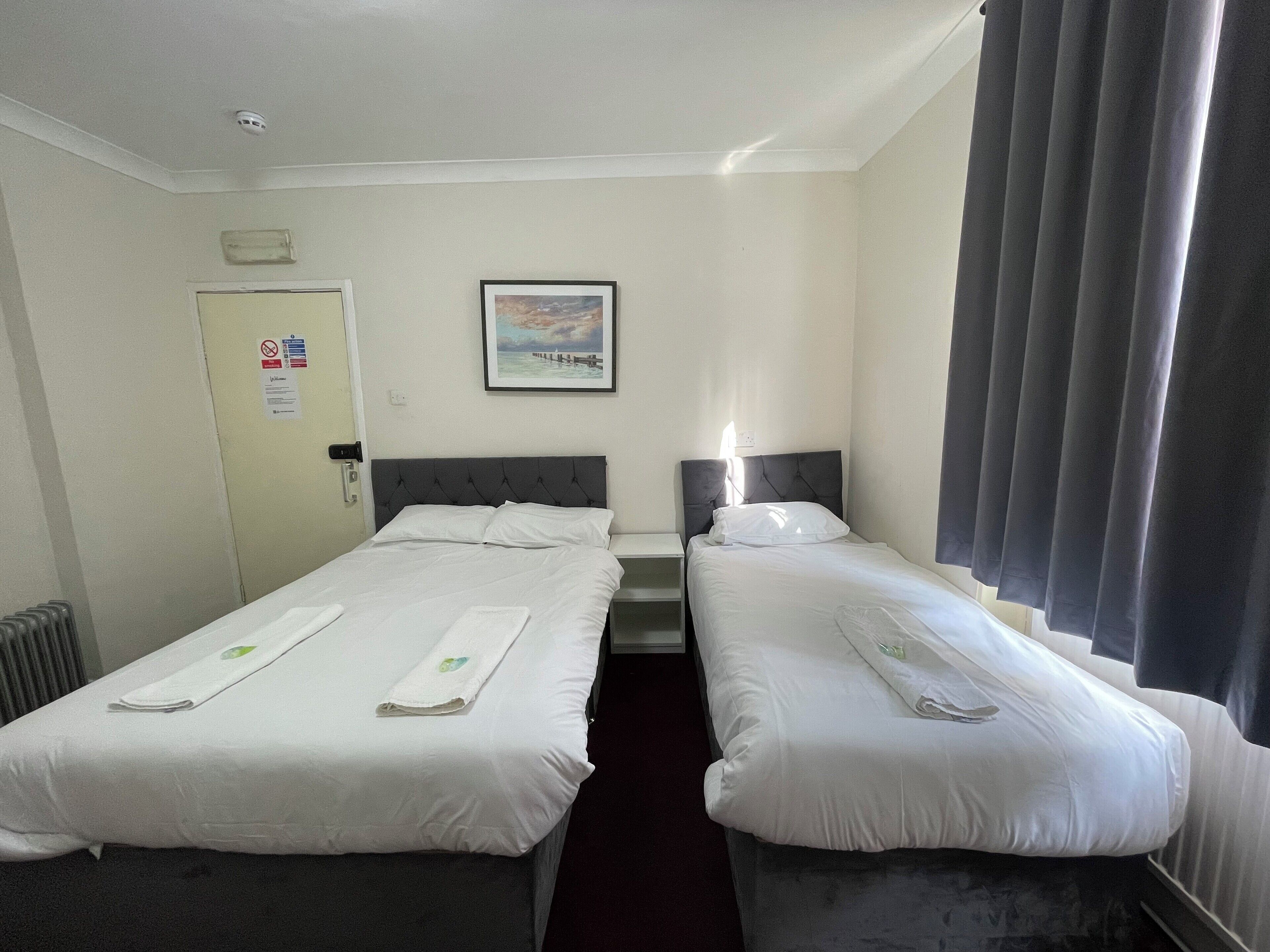 A hotel room with two single beds, a framed picture on the wall, a door with a sign, and a window with curtains.