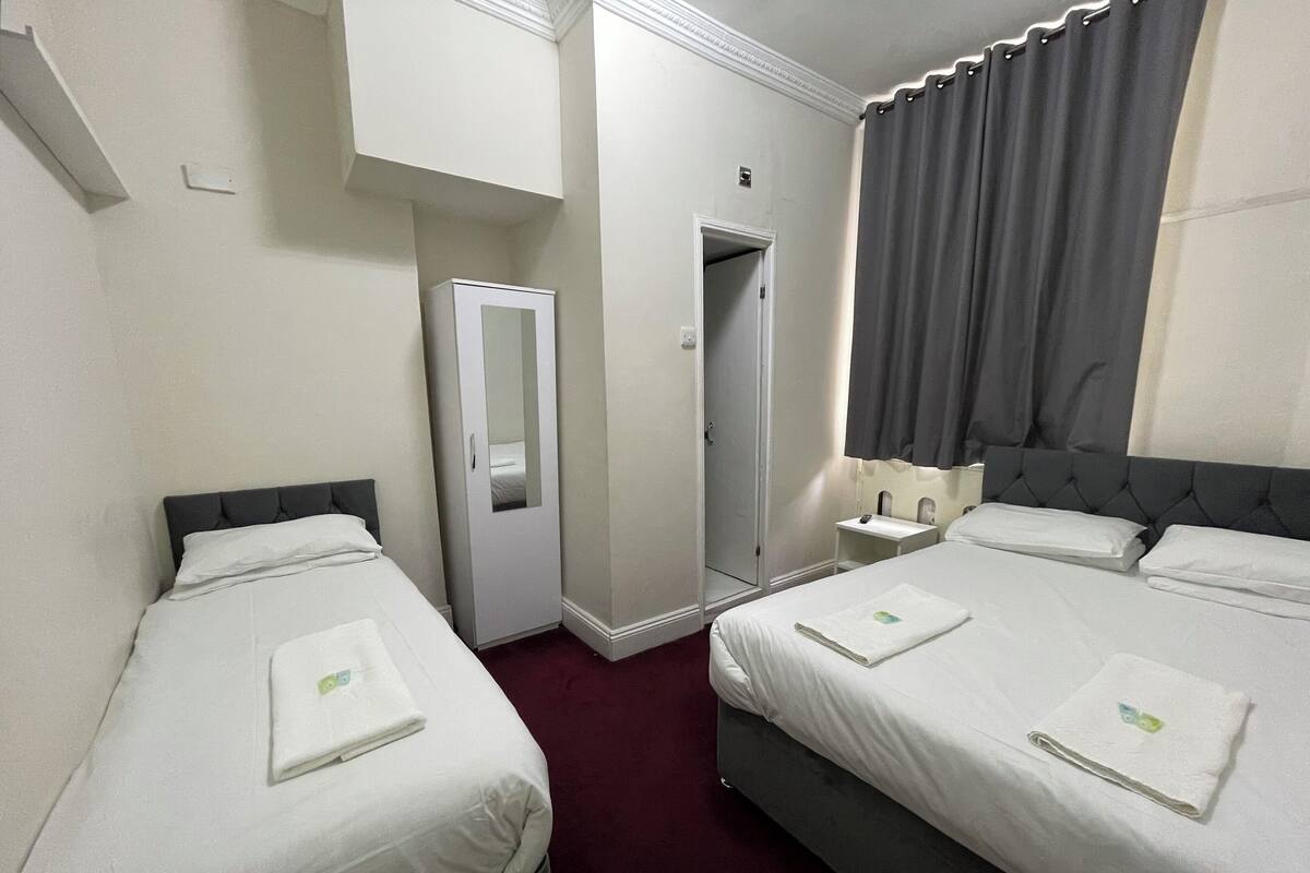 A hotel room with two beds, a wardrobe, a mirror, a nightstand, and a door leading to a bathroom.