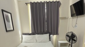 A hotel room with a bed, a flat-screen TV mounted on the wall, a standing fan, and a window with curtains. - Oban Victoria Hotel (London)
