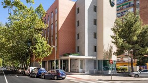 A multi-story hotel with a prominent B&B sign, a clear sky, and parked cars along the street. - B&B HOTEL Zaragoza Plaza Mozart  (Zaragoza)
