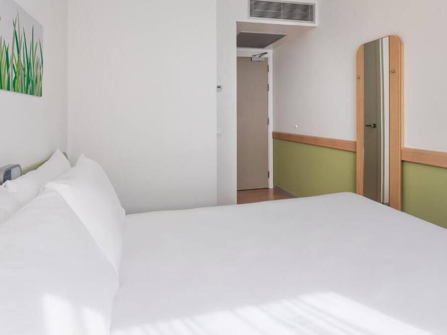 Une chambre d’hôtel avec un lit, un tableau au mur, une porte et un couloir.