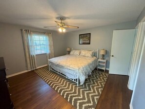 A bedroom with a bed, a ceiling fan, a window with curtains, a door, and a rug.