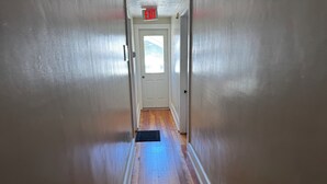 Un pasillo con suelo de madera, paredes blancas y una puerta al final.