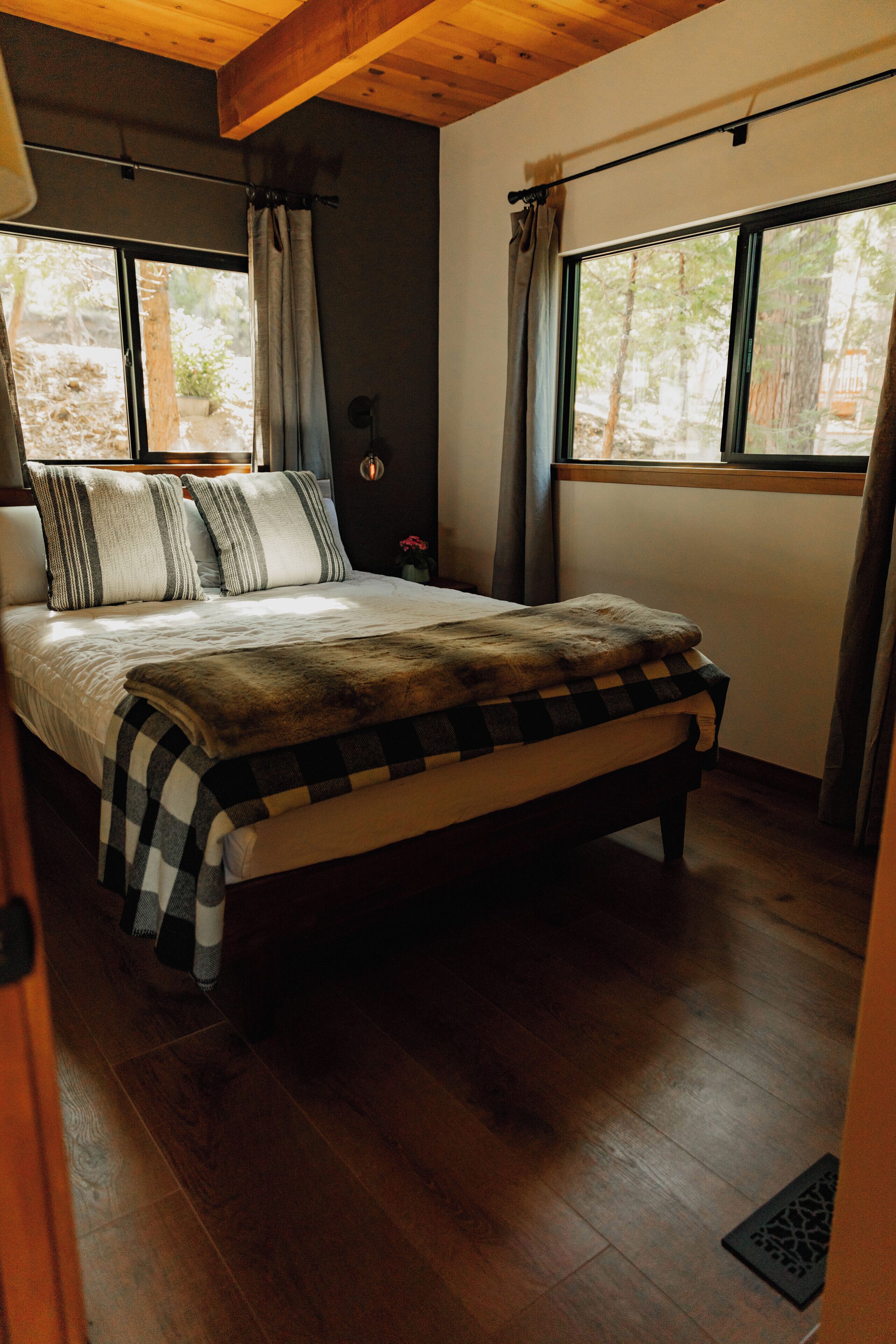 Un dormitorio con cama, suelo de madera y ventana con cortinas.
