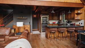 Ein geräumiger Wohnbereich mit einer großen Couch, einer Küche mit Holzschränken, einem Einbauofen und einer Bar mit Hockern.