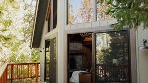 Ein modernes Haus mit einer Holzdiele, großen Schiebeglastüren, die in ein Schlafzimmer führen, und Blick auf Bäume.