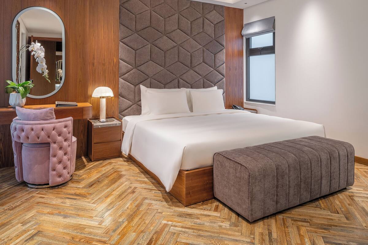 Una habitación de hotel moderna con una cama grande, cabecera de madera, tocador con espejo y suelo con estampado de espiga.