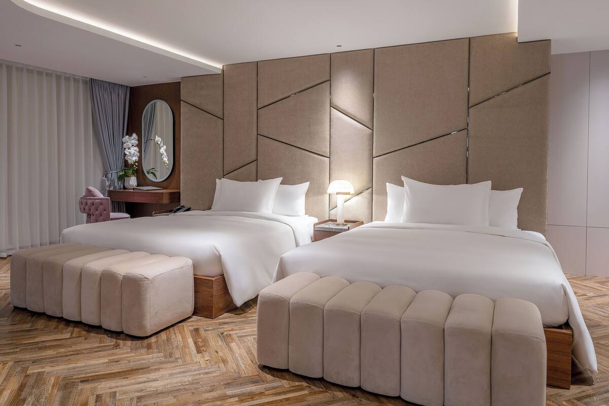 Una habitación de hotel moderna con dos camas, suelo de madera con diseño espiga y un espejo grande en la pared.