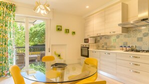 A modern kitchen with a glass dining table, yellow chairs, and a view of a balcony with greenery. - Marte, vacation apartment 100 m from Marina beach (Marina di Ragusa)