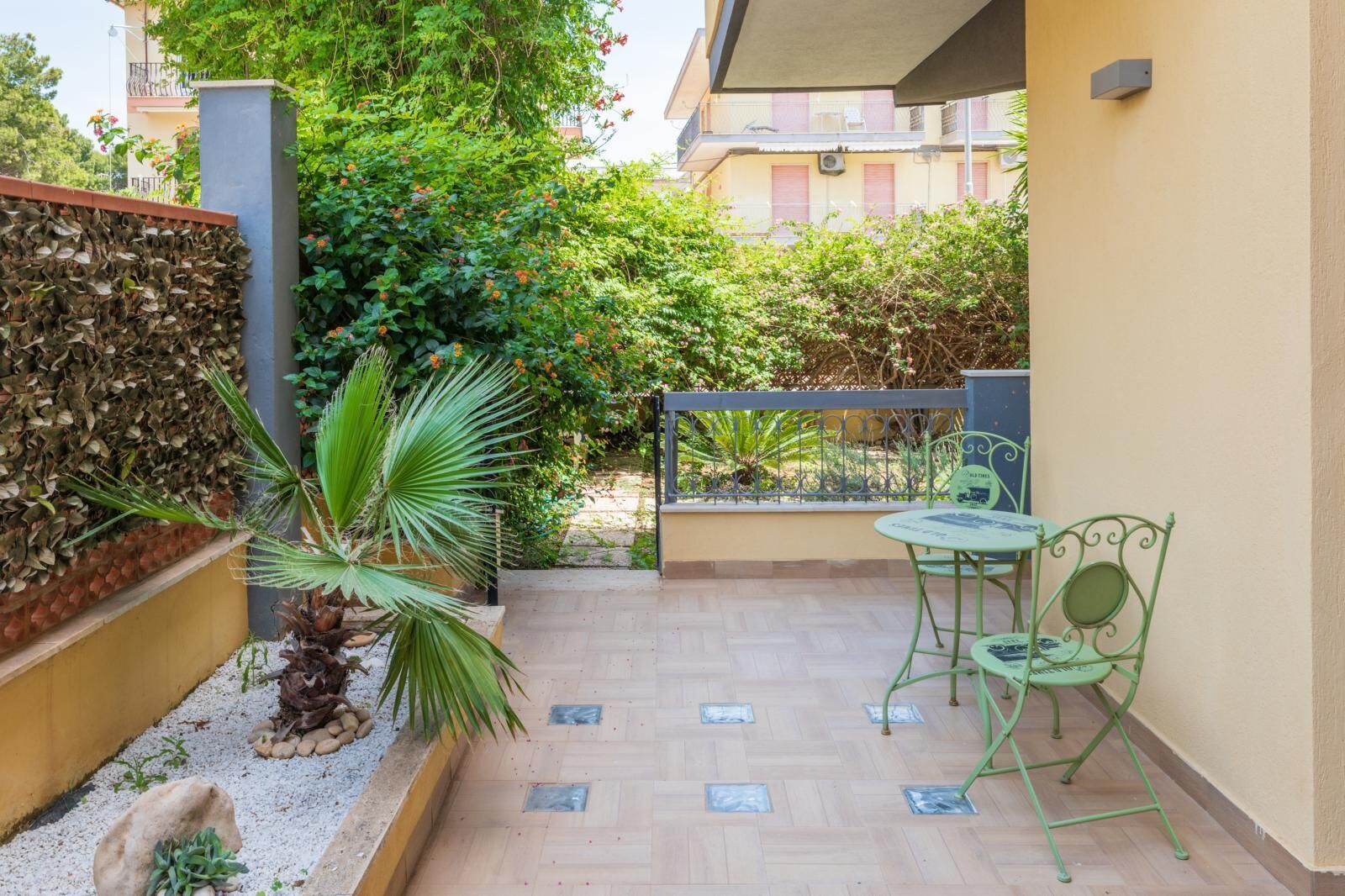 Un petit espace extérieur aménagé en patio, avec un sol en bois, un palmier et une table en métal entourée de chaises.