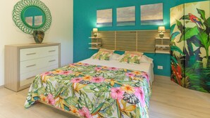 A bedroom with a bed, a dresser, a mirror, and a tropical-themed wall. - Marte, vacation apartment 100 m from Marina beach (Marina di Ragusa)