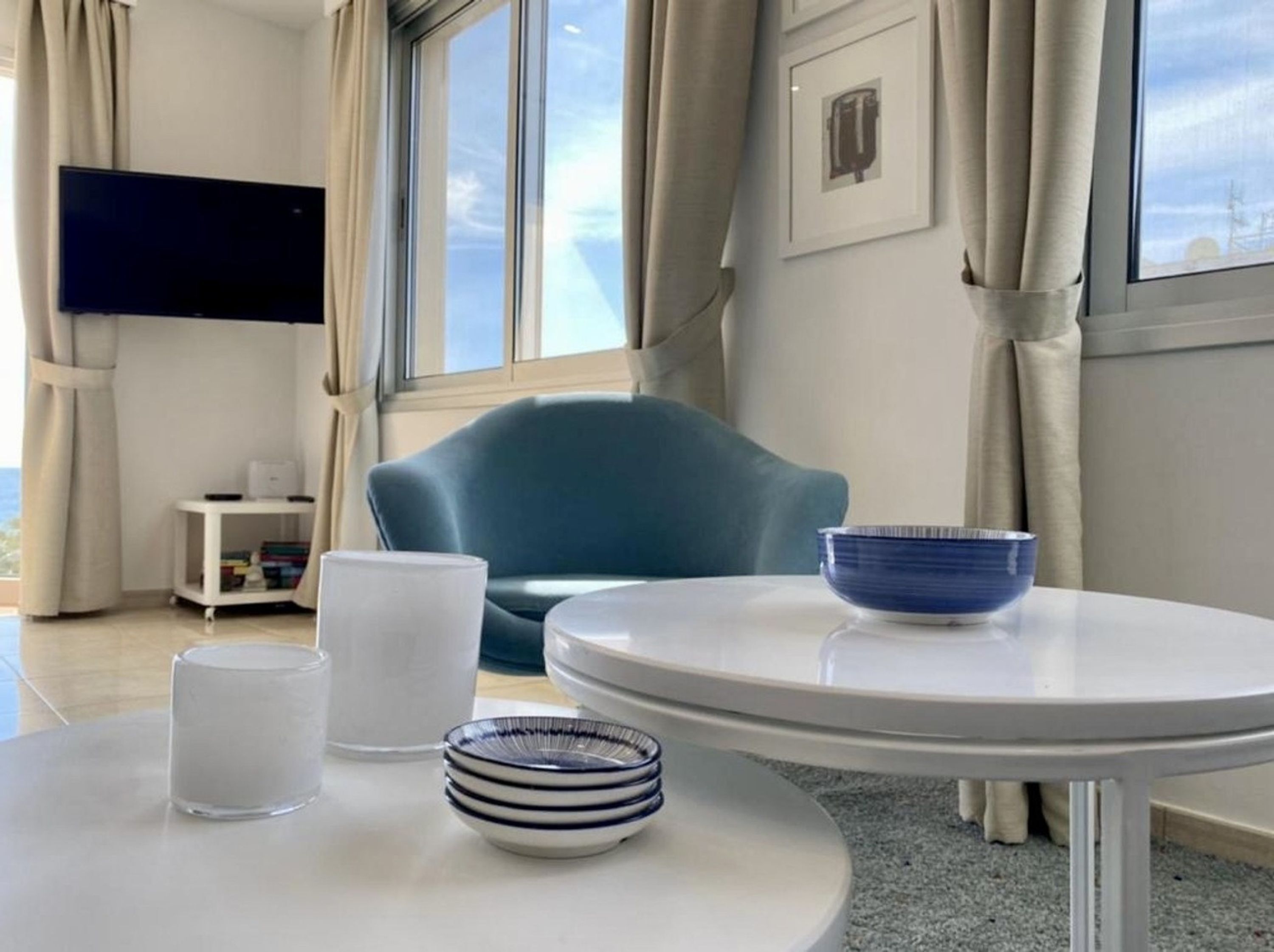 A modern room with a round table, a blue chair, a white lamp, and a TV on the wall.