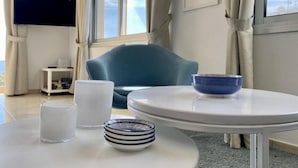 Una habitación moderna con una mesa redonda, una silla azul, una lámpara blanca y un televisor en la pared.