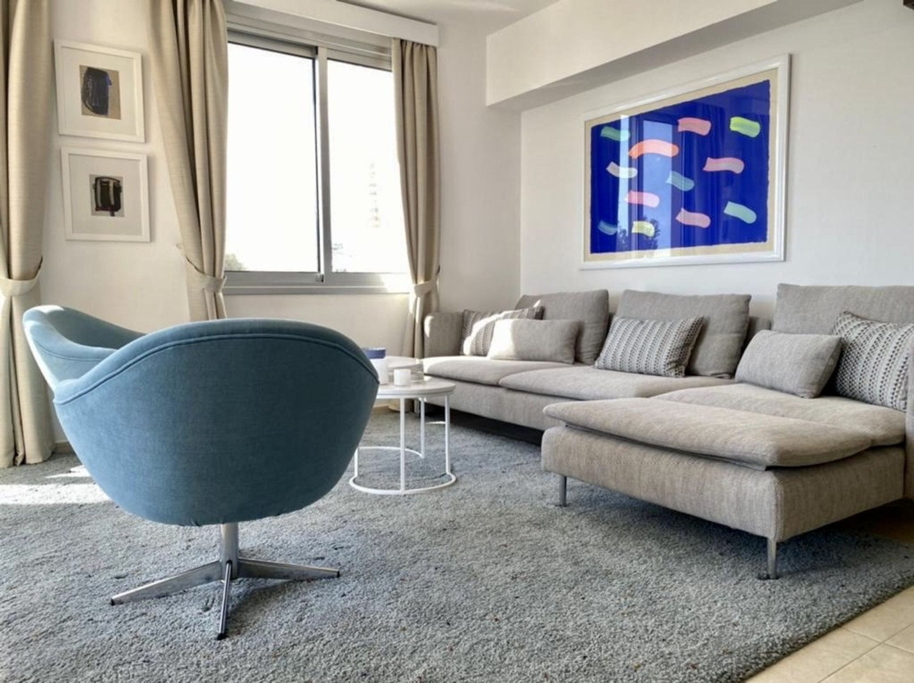 A modern living room with a blue chair, a grey sofa, and a large abstract painting on the wall.