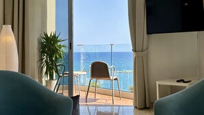 Una habitación de hotel con balcón, televisor montado en la pared y una planta en maceta.