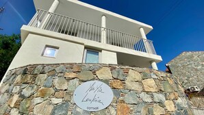 Een gebouw met twee verdiepingen, een stenen gevel en een balkon. Op de stenen muur staat een bordje met de tekst 'Via Via Lontia COTTAGE'.