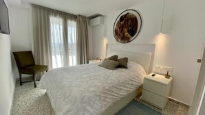 Een slaapkamer met een groot bed, twee nachtkastjes, een stoel en een kunstwerk aan de muur.
