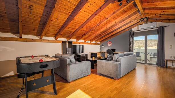 Un'ampia zona giorno con soffitto in legno, divani grigi, tavolo da biliardo e un balcone con vista.