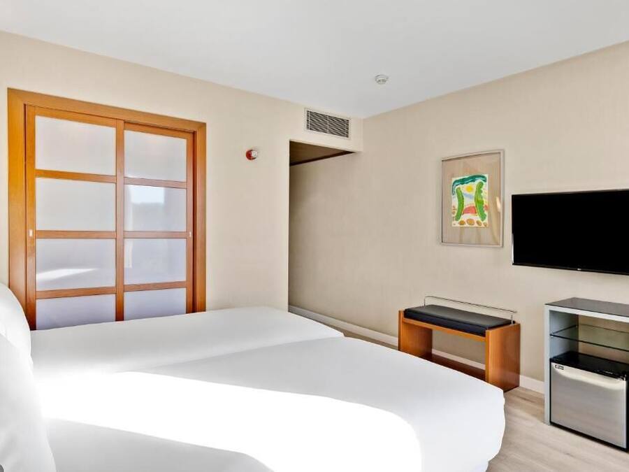 A hotel room with a bed, a desk, a television, and a window.
