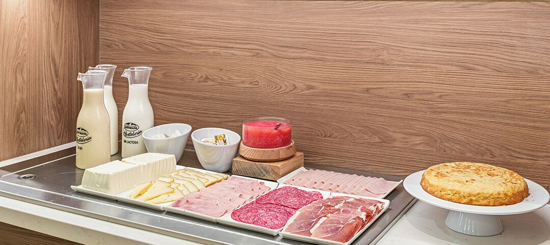 Een ontbijtplateau met diverse vleessoorten, kazen en een taart op een houten tafel.