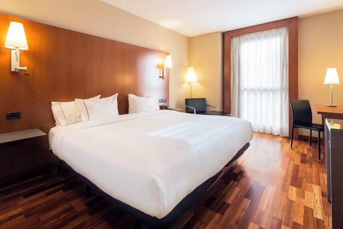 A hotel room with a large bed, two bedside tables, a desk, and a chair.