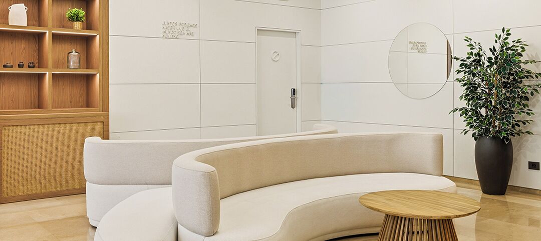 A modern interior with a curved sofa, a round wooden table, a potted plant, and a wooden cabinet with shelves.