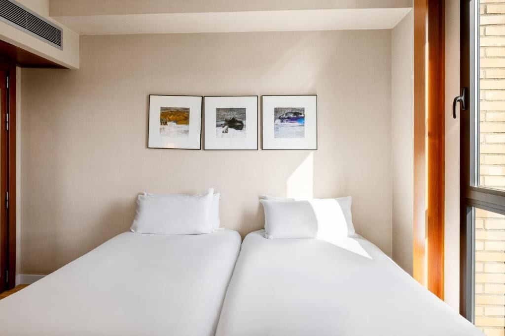 A hotel room with two beds, a window, and three framed pictures on the wall.