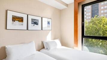 Ett hotellrum med två sängar, ett stort fönster och tre inramade tavlor på väggen.