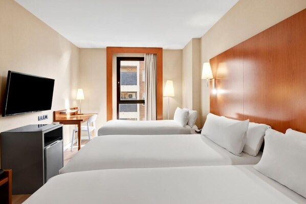 Une chambre d’hôtel avec deux lits, une télévision, un bureau et une fenêtre avec des rideaux.