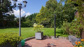 Ein Gartenpfad mit Rasenfläche, einer Straßenlaterne und einem großen Pflanzgefäß mit weißen Blüten.