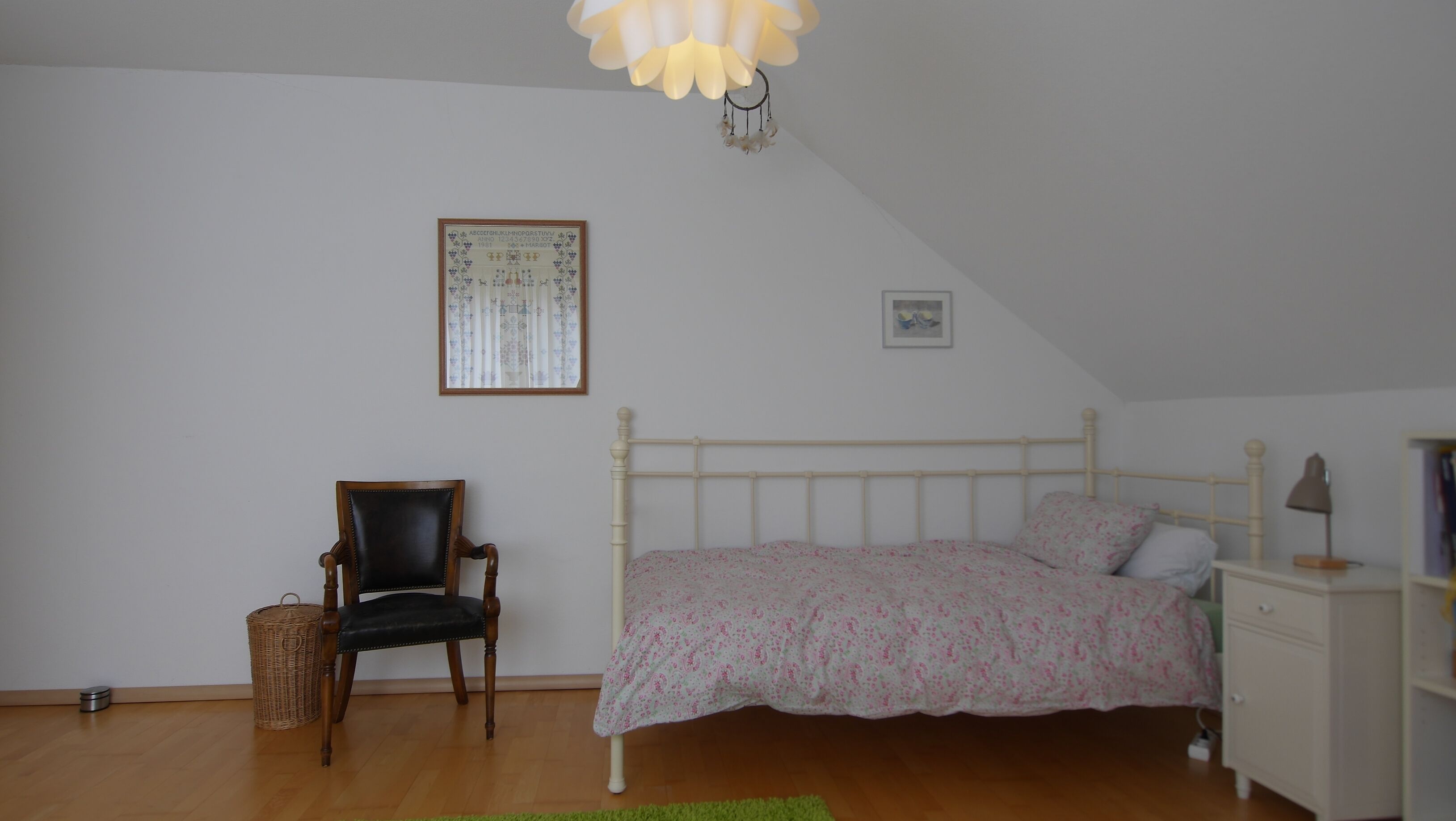 Um quarto com uma cama, uma cadeira, uma mesinha de cabeceira, um abajur e um lustre.
