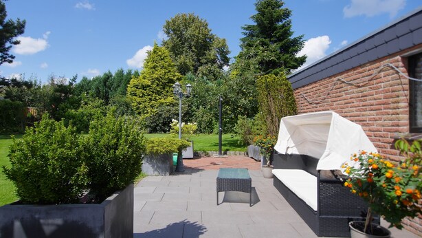 Ein Außenbereich mit Terrassengarten, überdachter Sitzgelegenheit, Backsteinmauer und diversen Blumentöpfen.