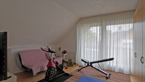 Ein Schlafzimmer mit Bett, Ergometer, Sitzbank und Heizkörper.