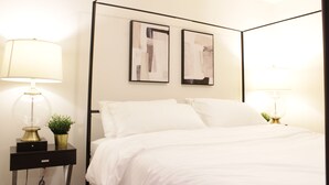 A neatly made bed with white linens, two bedside lamps, and two abstract wall art pieces. - Brand New| 3 Bedroom, 1 king 2 Queen| Near Airport (Calgary)