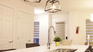 A modern kitchen with a large island, stainless steel sink, and a hanging light fixture. - Brand New| 3 Bedroom, 1 king 2 Queen| Near Airport (Calgary)