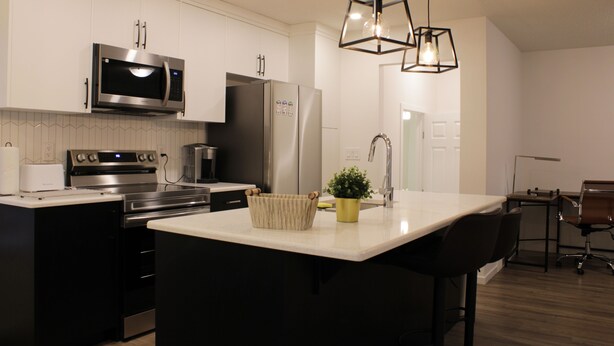 A modern kitchen with stainless steel appliances, a central island, and pendant lighting. - Brand New| 3 Bedroom, 1 king 2 Queen| Near Airport (Calgary)