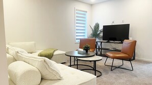 A living room with a sofa, two chairs, a coffee table, a TV, and a plant. - Brand New| 3 Bedroom, 1 king 2 Queen| Near Airport (Calgary)