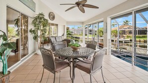 Une terrasse ensoleillée avec une table ronde, des chaises et un ventilateur de plafond.