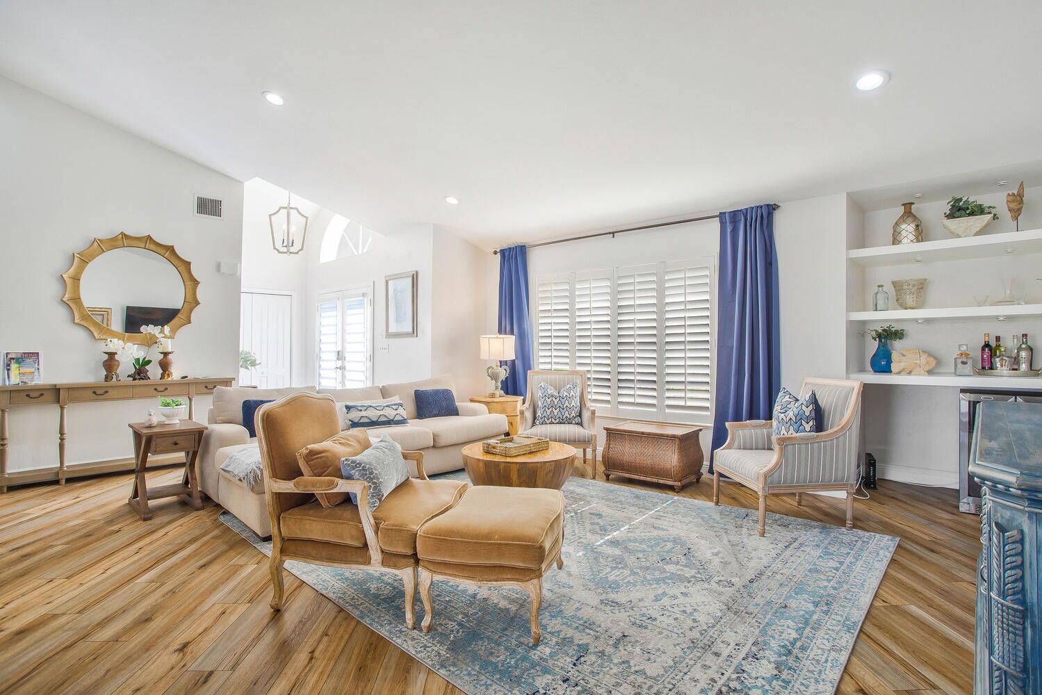 A spacious living room with a wooden floor, a large mirror, a sofa, a coffee table, and a dining area with a white shelf.