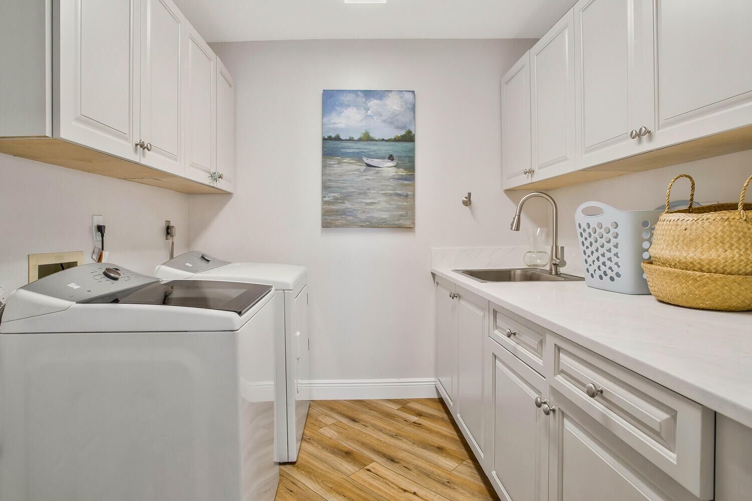 A compact kitchen with a washing machine, a sink, and a painting of a lake scene.