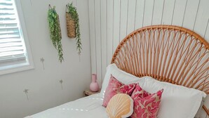 Un lit avec une couverture à rayures, une tête de lit en osier et un vase rose sur la table de chevet.