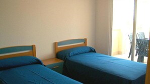 A room with two beds, a small table, and a chair near a sliding glass door. - Mercury (Peniscola)