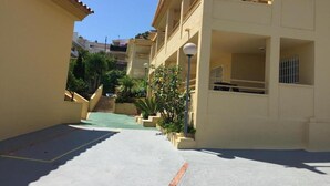 A narrow courtyard with a staircase leading to a second floor, surrounded by buildings with balconies and outdoor plants. - Mercury (Peniscola)