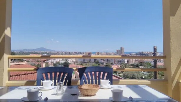A balcony with a table set for two, overlooking a cityscape with buildings and a mountain in the distance. - Mercury (Peniscola)