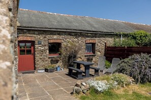 A stone cottage with a red door, a small window, and a patio area with a table and chairs. - Swallows Cottage comfy & cosy traditional cottage (SOLVA, HAVERFORDWEST)