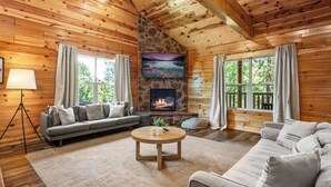 L’intérieur chaleureux d’un chalet avec une cheminée en pierre, des murs en bois, un canapé et une table basse.