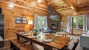 L’intérieur d’un chalet en bois comprend une table à manger pour quatre personnes, un canapé, une cheminée et un mur en pierre.