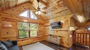 L'intérieur d'un chalet en bois, avec un canapé, un téléviseur et un ventilateur de plafond.
