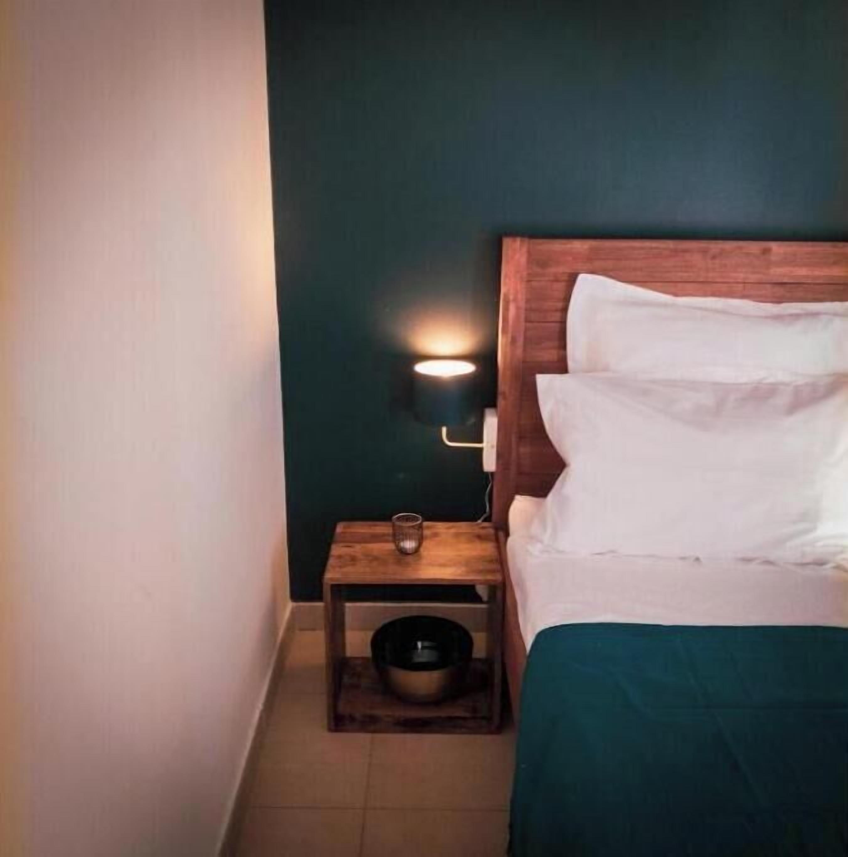 Un dormitorio con cabecera de madera, una mesita de noche con lámpara y un cuenco en el suelo.